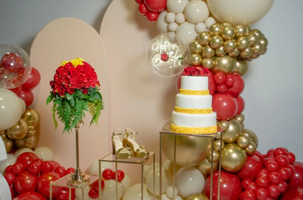 Red and gold balloon arch with a tiered cake and floral display at Event Center Miami