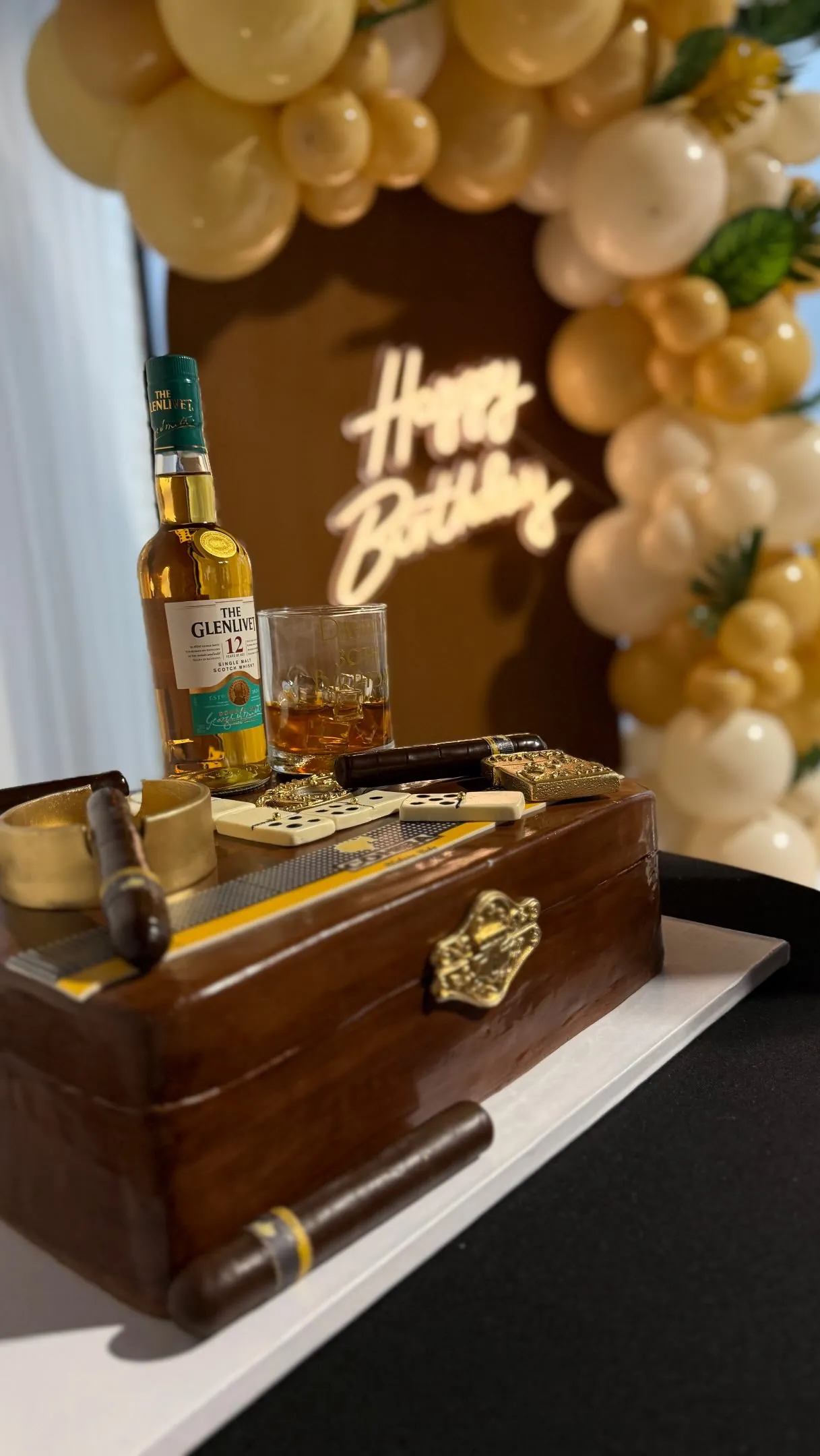 Whiskey and cigar themed birthday lounge under a gold balloon arch