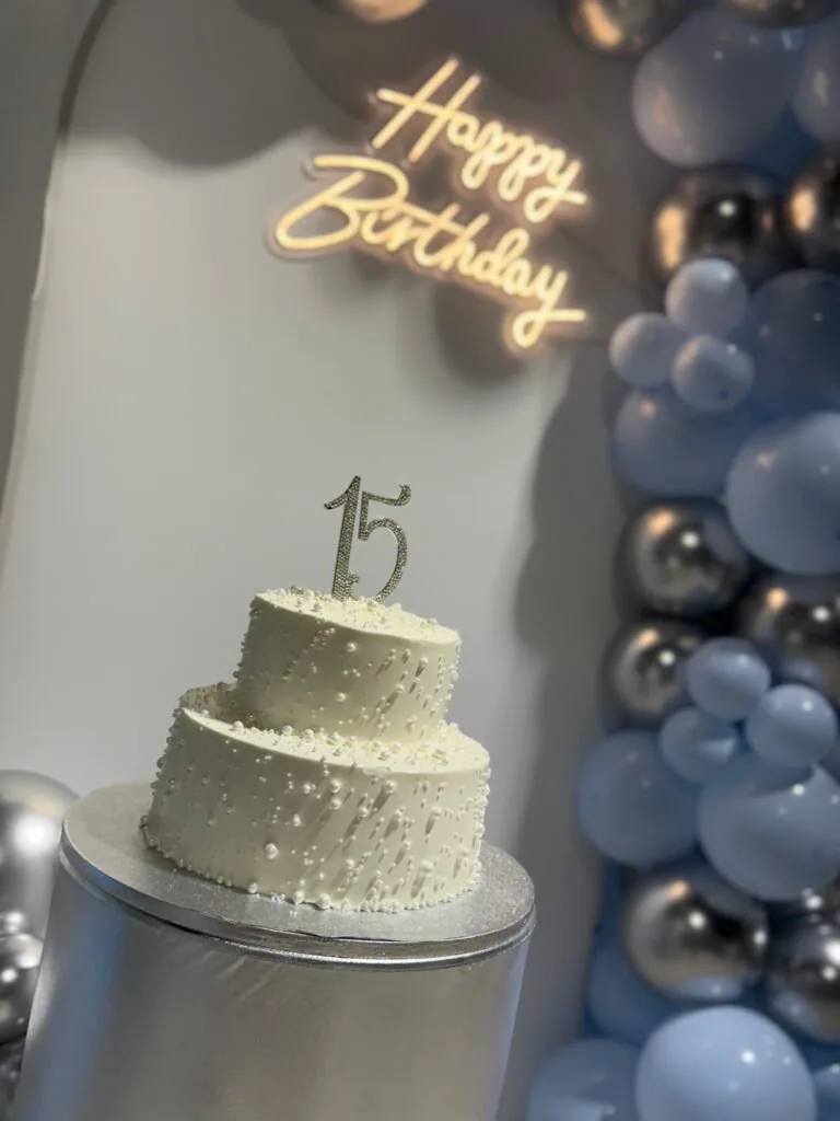 Tiered birthday cake with a Happy Birthday neon sign and blue balloon garland at Event Center Miami